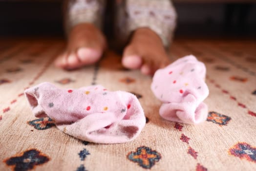 Pair of children's fluffy, pink, polka-dotted socks on patterned carpet, child in pajamas in background.