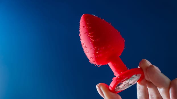Woman holding red anal plug in water drops on blue background