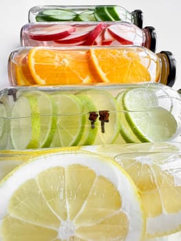 Stacked glass bottles with detox drinks with cucumber, apple, orange, and lemon slices on white background. Vertical orientation, refreshing beverage concept for design and print. High quality photo