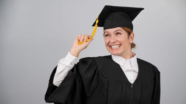 Smiling woman in graduation gown holding cap by tassel on white background