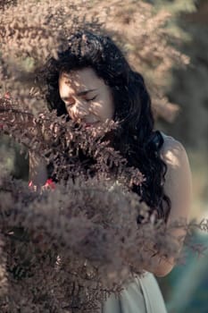 A woman is standing in a field of brown leaves. She is looking at the camera with a serious expression