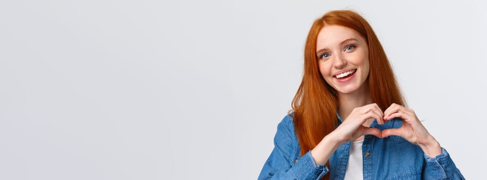 Happy valentines day, love. Cute and tender romantic redhead girlfriend showing heart sign, confess in sympathy, express passion or like, admire amazing artwork, appreciate, stand white background.