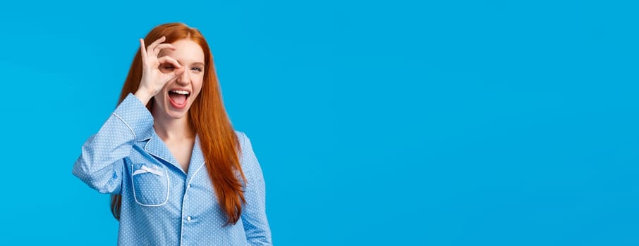 Carefree and sassy happy redhead woman with blue eyes, showing okay, no worries and satisfaction gesture over eye, look through fingers pleased, showing tongue, promote feminine hygiene products.