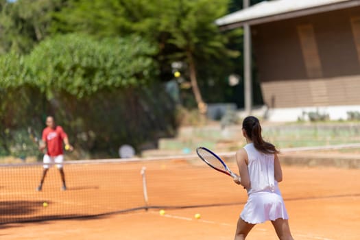 A woman is playing tennis with a man. The woman is wearing a white skirt and is holding a tennis racket