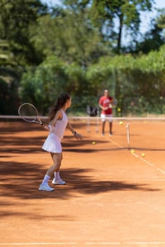 A woman is playing tennis on a clay court. A man is watching her play. The woman is wearing a white shirt and a white skirt