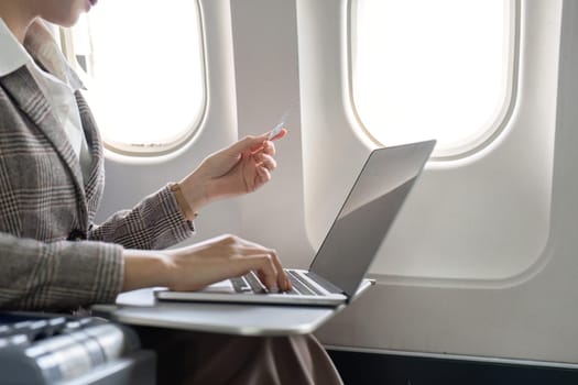 Businesswoman making online purchase on laptop during flight, Concept of in-flight productivity