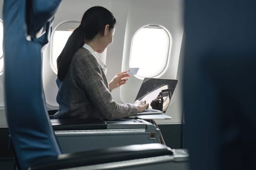 Businesswoman seated on airplane using laptop for an online purchase, illustrating work-life balance and in-flight productivity