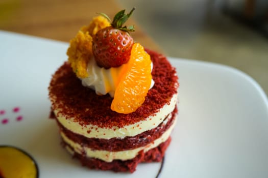 Red velvet cake, classic three layered cake from red butter sponge cakes with cream cheese frosting, with mandarin orange and candied strawberry as topping American cuisine cooking content creation