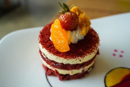 Red velvet cake, classic three layered cake from red butter sponge cakes with cream cheese frosting, with mandarin orange and candied strawberry as topping American cuisine cooking content creation