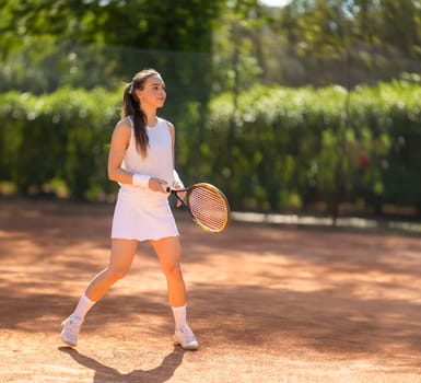 A woman is playing tennis on a clay court. She is wearing a white skirt and a white top