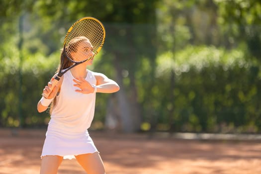 A woman is playing tennis on a court. She is wearing a white dress and holding a tennis racket
