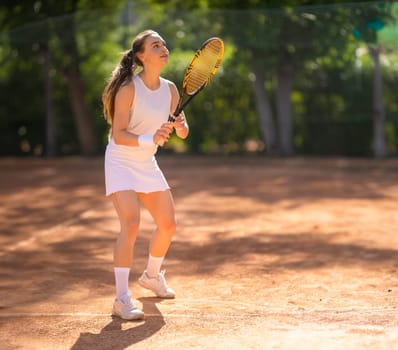 A woman is playing tennis on a clay court. She is wearing a white shirt and white shorts