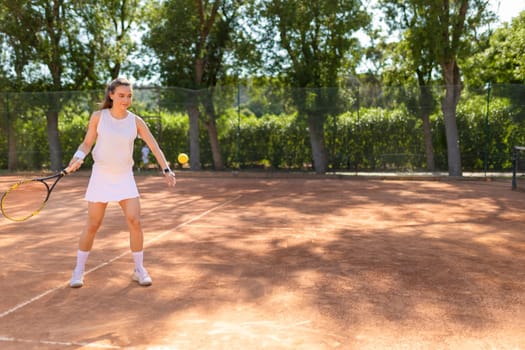 A woman is playing tennis on a clay court. She is holding a tennis racket and is about to hit a yellow ball