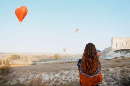 Woman admiring colorful hot air balloons flying over stunning landscape in cappadocia, turkey