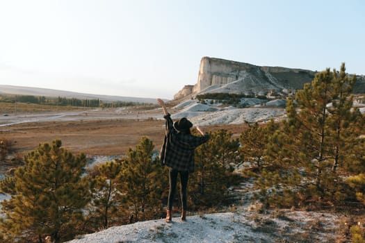 Triumphant woman on mountaintop gazes at majestic landscape with arms raised in victory