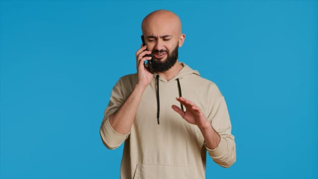 Middle eastern guy chatting with friends on phone call, answering smartphone while standing over blue background. Modern man discussing something on a remote network. Camera 1.