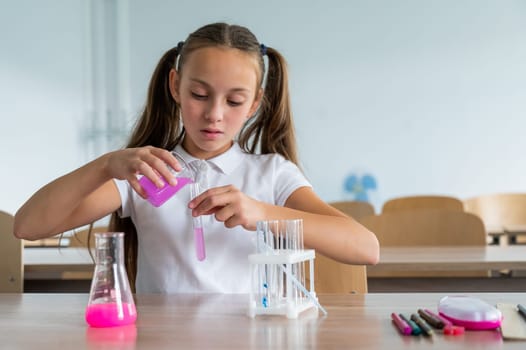 A schoolgirl conducts experiments in a chemistry lesson. Girl pouring colored liquids from a beaker