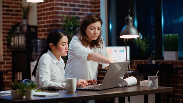 Asian staff member calling manager to her computer desk to ask for feedback on project progress. Worker in brick wall office requesting assistance from team leader during nightshift