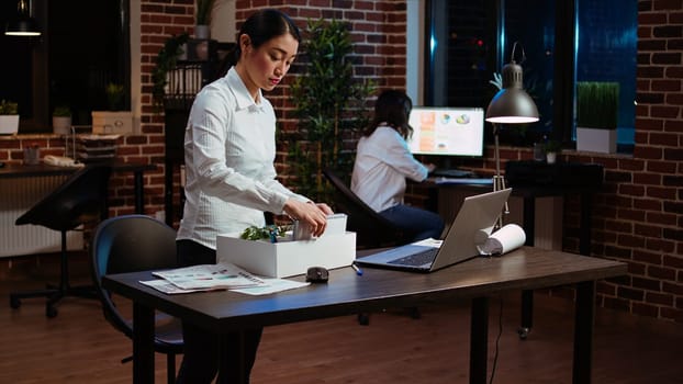 Sad employee packing desk things after quitting job, saying goodbye to colleague. Disappointed employee preparing to leave workplace after accepting another company position, camera A