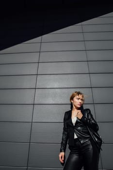 a woman in black leather clothing fashion style against the background of a dark wall