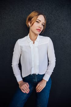 beautiful woman in a white blouse stands against a dark wall