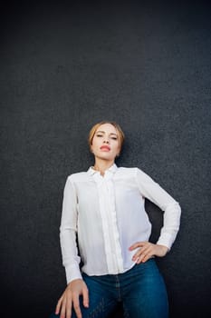 beautiful woman in a white blouse stands against a dark wall