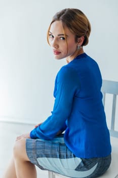 a woman in business blue suit sits on a chair in a bright office