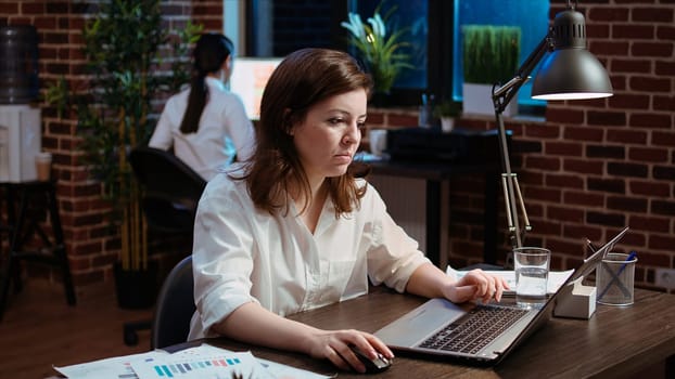 Smiling staff member planning marketing project on laptop late at night, pleased by ideas. Office employee working nightshift, satisfied with company development strategy she came up with