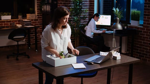 Frustrated employee packing desk belongings after being fired, saying goodbye to coworker. Upset employee preparing to leave office after being discharged by company management, camera A