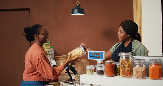 Client buying various pasta and grains in jars from organic shop, supporting local farming business and sustainable lifestyle. Vegan woman looking for chemicals free food essentials. Handheld shot.