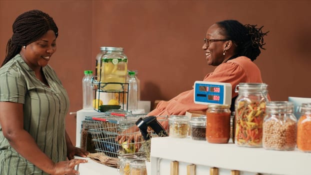 African american vendor selling freshly harvested produce to frequent customer at local zero waste eco store. Vendor placing organic fruits and vegetables on scale at cash register.