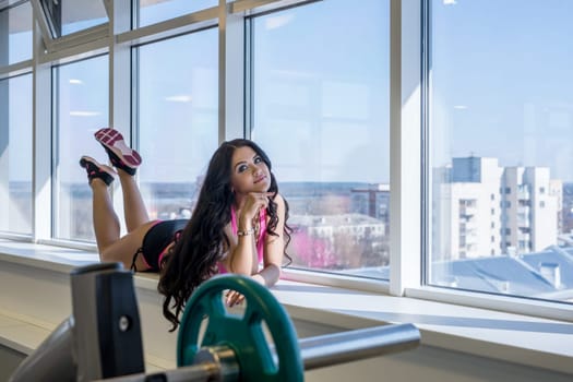 At gym. Athletic young brunette posing on window sill