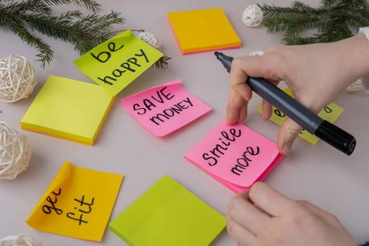 Unrecognizable woman writing new year's resolutions on colorful sticky notes. Making promises for new year, setting goals. Creating vision board motivation