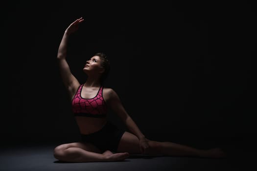 Studio photo of graceful brunette exercising in dark