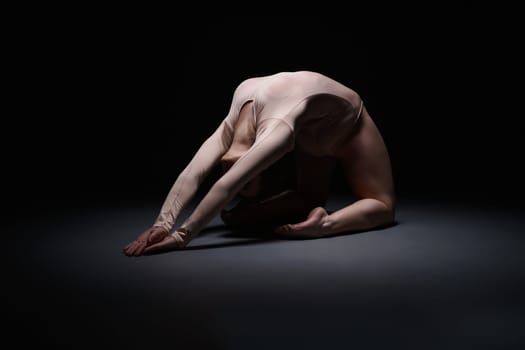 Flexible female gymnast posing while exercising in dark studio