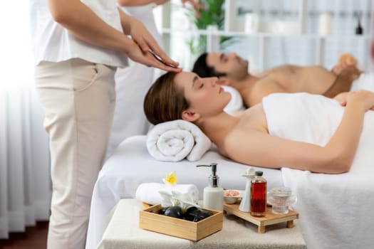 Caucasian couple enjoying relaxing anti-stress head massage and pampering facial beauty skin recreation leisure in dayspa modern light ambient at luxury resort or hotel spa salon. Quiescent