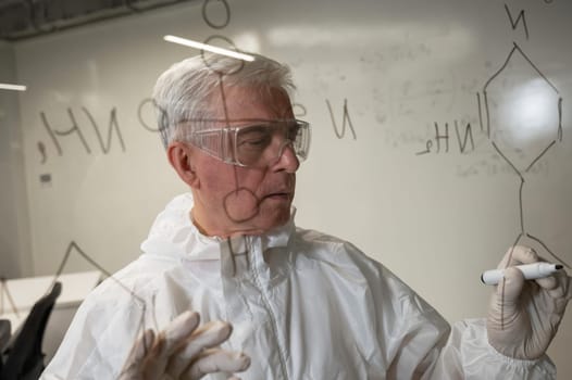 An elderly Caucasian male chemist in a protective suit writes on glass