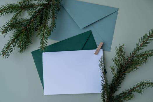 Green background with Christmas tree branch decor and copy space mock up white envelope. Template for Christmas greeting card New Year postcard. Flat lay top view