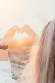 A woman's hand is holding a heart shape, with the sun shining on it. Concept of love and warmth, as the sun symbolizes happiness and positivity. The heart shape represents the bond between two people