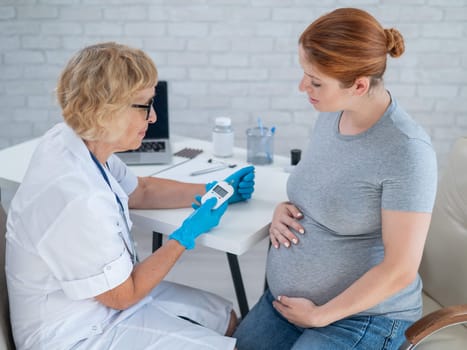 An elderly female doctor checks the blood sugar level of a pregnant red-haired woman. Gestational diabetes