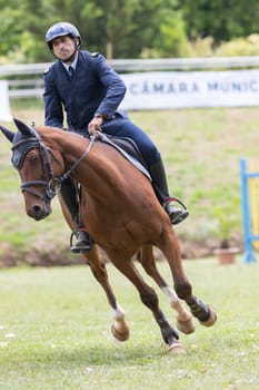 19 may 2024, Mafra, Portugal - competition in military academy - man is riding a brown horse in a field. The horse is running and the man is wearing a blue jacket