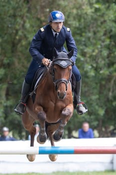 19 may 2024, Mafra, Portugal - competition in military academy - man in a blue suit is riding a brown horse over a jump. The man is wearing a helmet and is dressed in a uniform. The horse is jumping over a hurdle, and the man is in the air as well