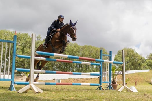 19 may 2024, Mafra, Portugal - competition in military academy - woman is riding a horse over a blue, white and red jump