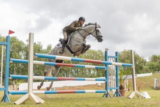 19 may 2024, Mafra, Portugal - competition in military academy - man is riding a horse over a blue and white hurdle. The horse is jumping over the obstacle with ease. The scene is lively and energetic, showcasing the skill and athleticism of both the rider