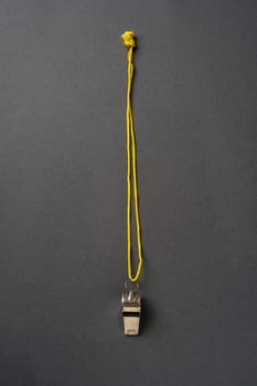 Top view of metal whistle with yellow string on dark gray background