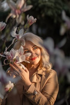 A woman is holding a magnolia flower in her hand and standing in front of a tree. Concept of serenity and beauty, as the woman is surrounded by nature and the flower adds a touch of color