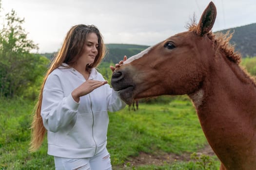 A woman is petting a brown horse in a field. The woman is wearing a white jacket and jeans