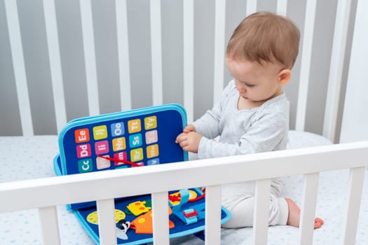 Little baby girl playing with busy book while sitting in crib. Concept of smart quiet books and modern educational toys