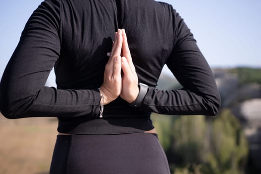 A woman is in a yoga pose with her hands on her hips. She is wearing a black shirt and black pants