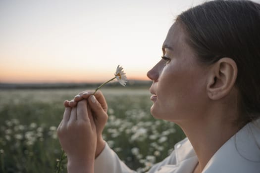 A woman is sitting in a field of flowers and smelling a white flower. The scene is peaceful and serene, with the woman enjoying the beauty of nature